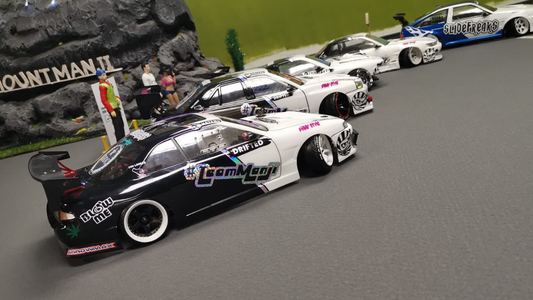 Line of scale RC drift cars staged on an indoor RC drift track, showcasing detailed body shells, wheels, and realistic drift setups